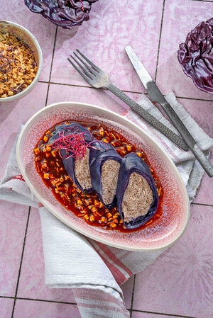 Red cabbage roulade served on a orange-red sauce, garnished with pink sprouts, and served side by side, sliced open.